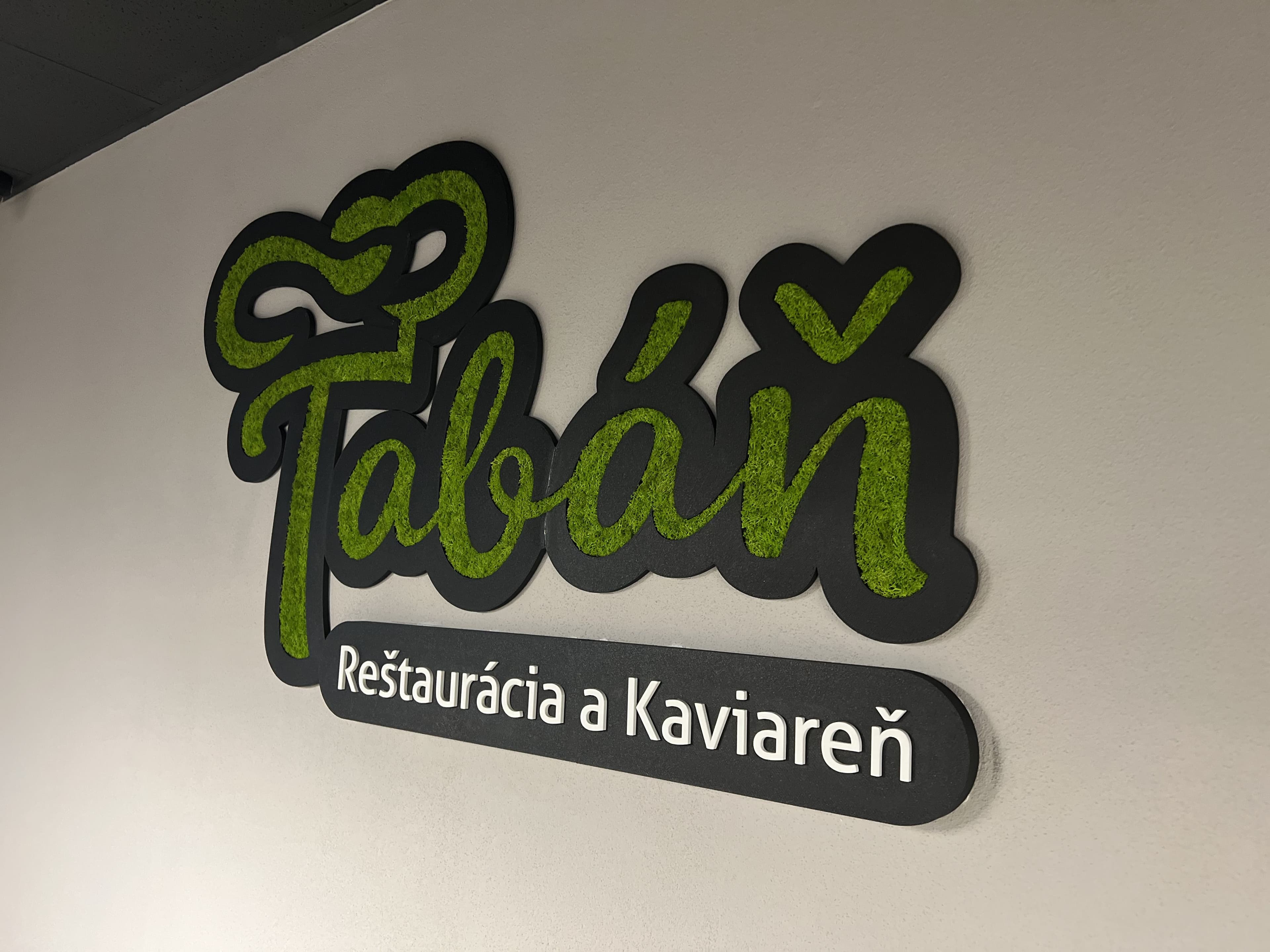 3D logo Tabáň – Reštaurácia a Kaviareň s machovou výplňou písmen na bielej stene