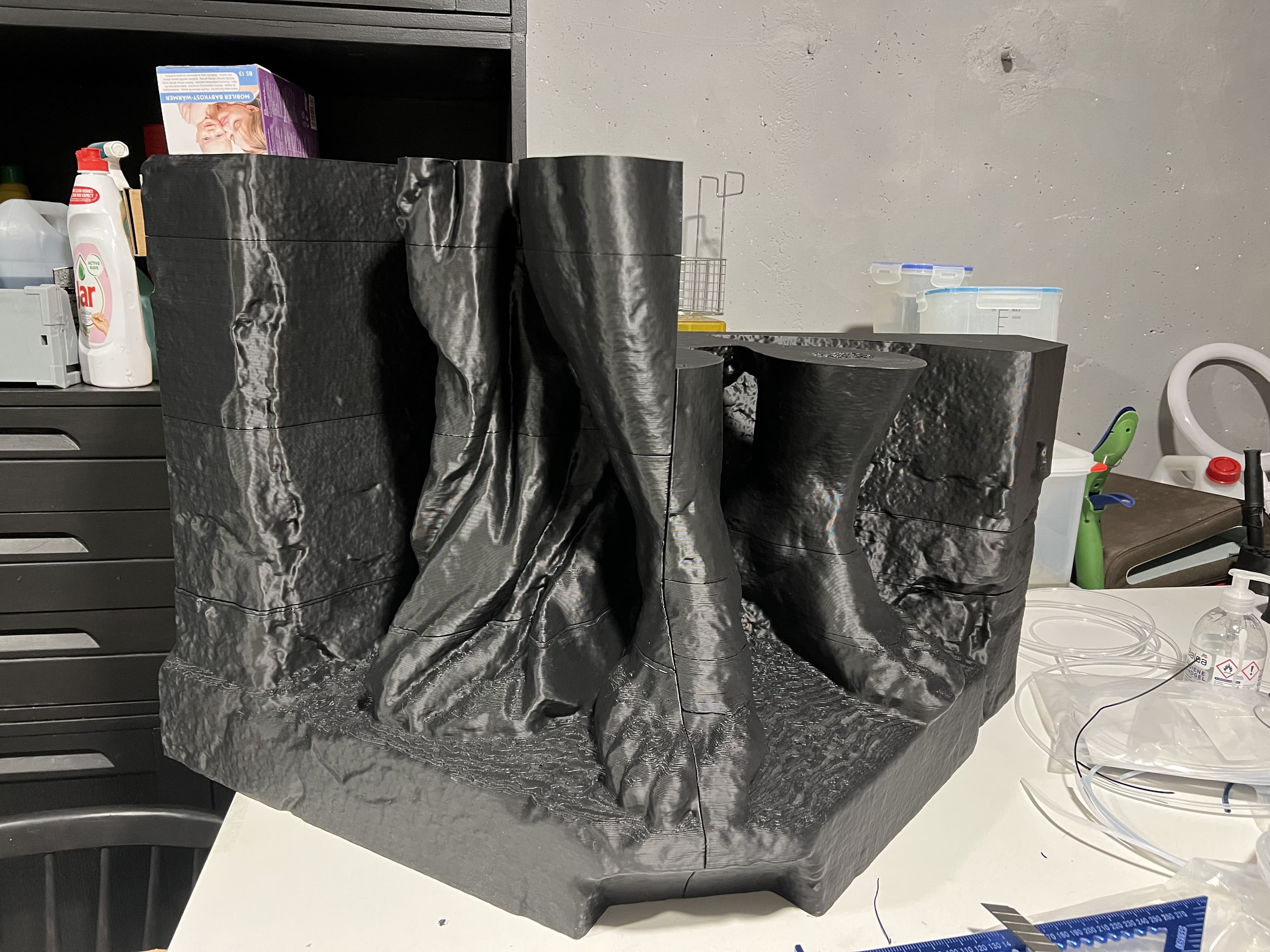 3D vytlačené segmenty nôh a plášťa sochy zo čierneho filamentu, zmontované na pracovnom stole